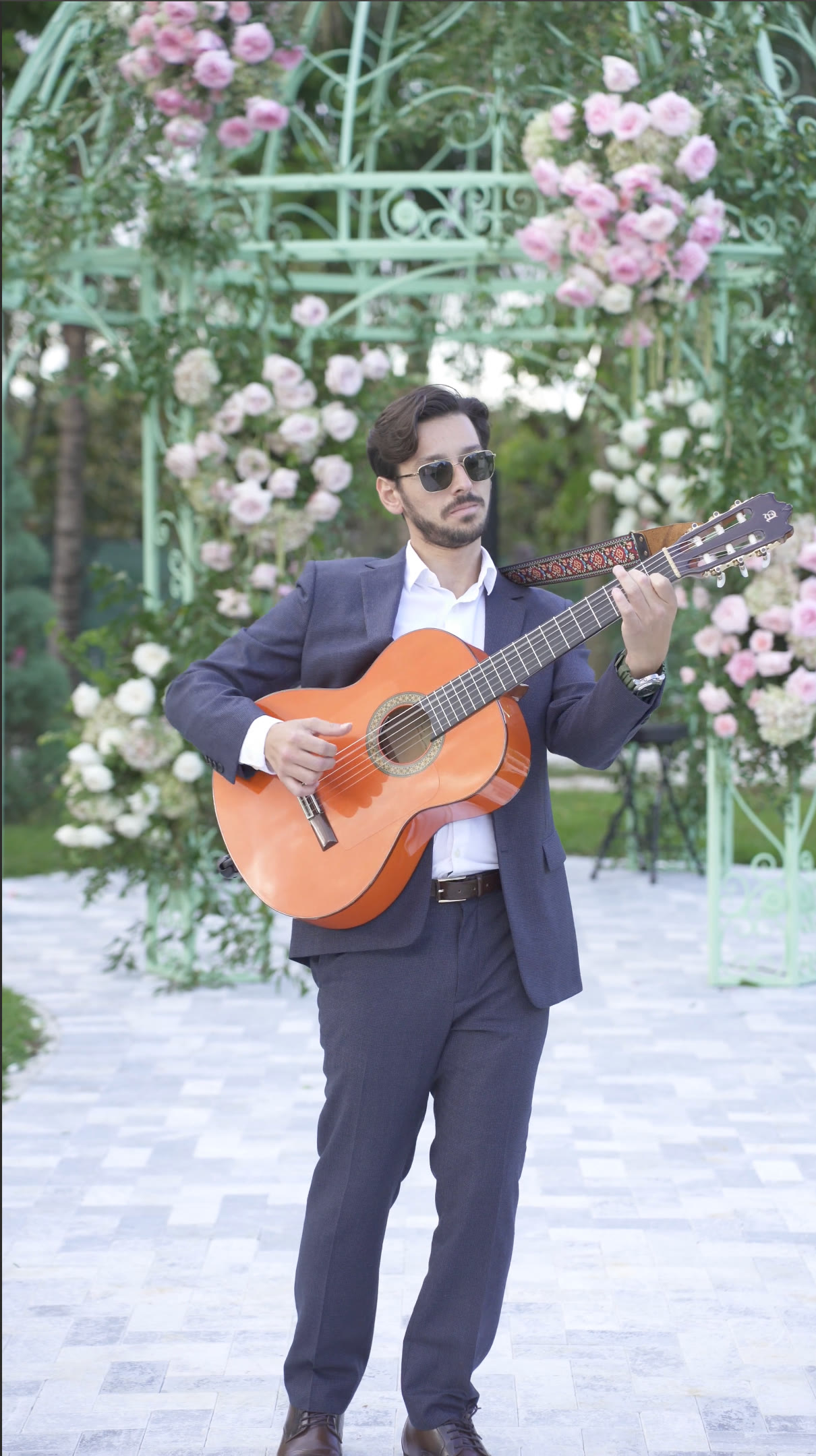 Sergio playing Spanish guitar beside a floral ceremony arch
